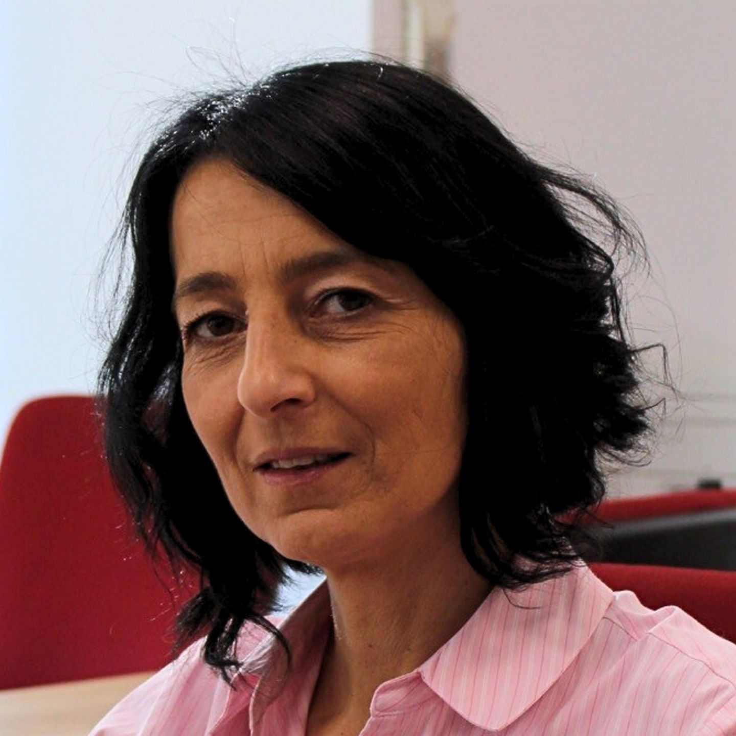 Cristina Pasere, Manager Compliance Operations Support la EOS România, stă la biroul ei într-o bluză cu dungi roz și se uită la cameră.