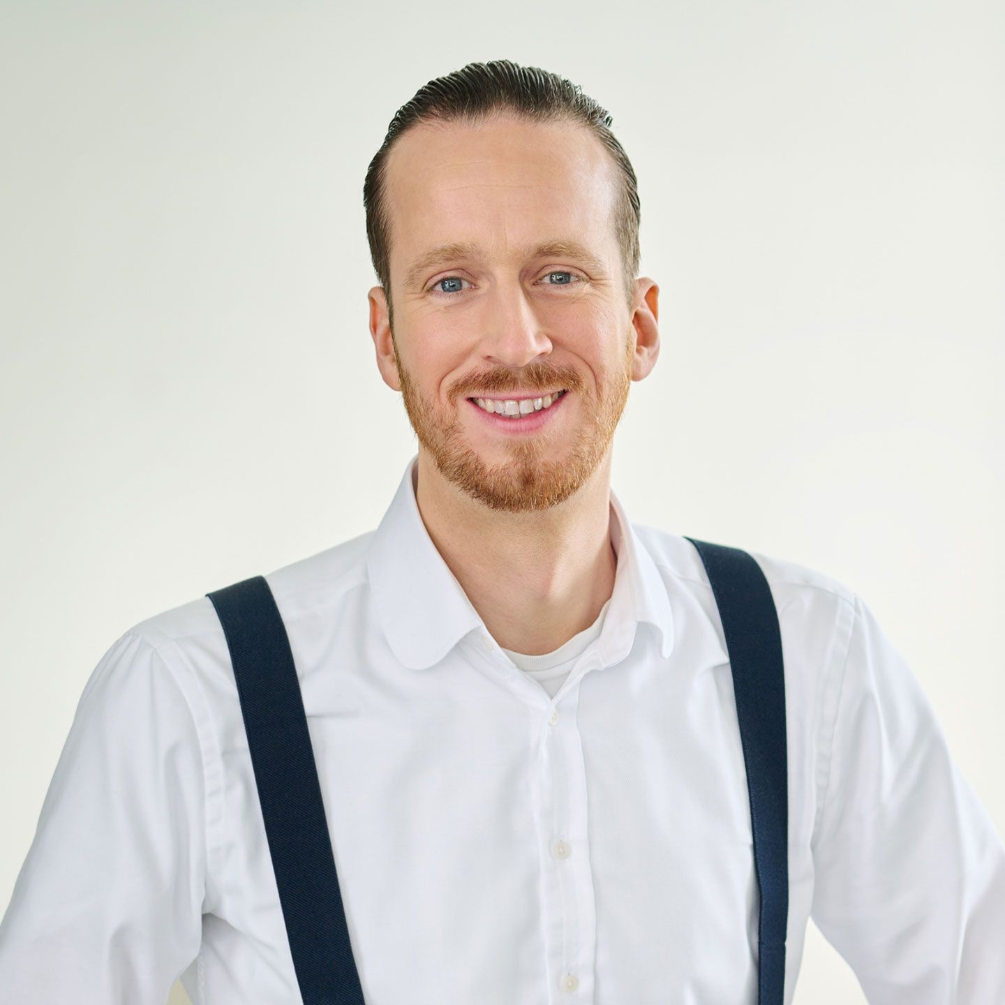 Sebastian Pollmer, un bărbat în cămașă albă și bretele albastre, stând într-o cameră luminoasă. 