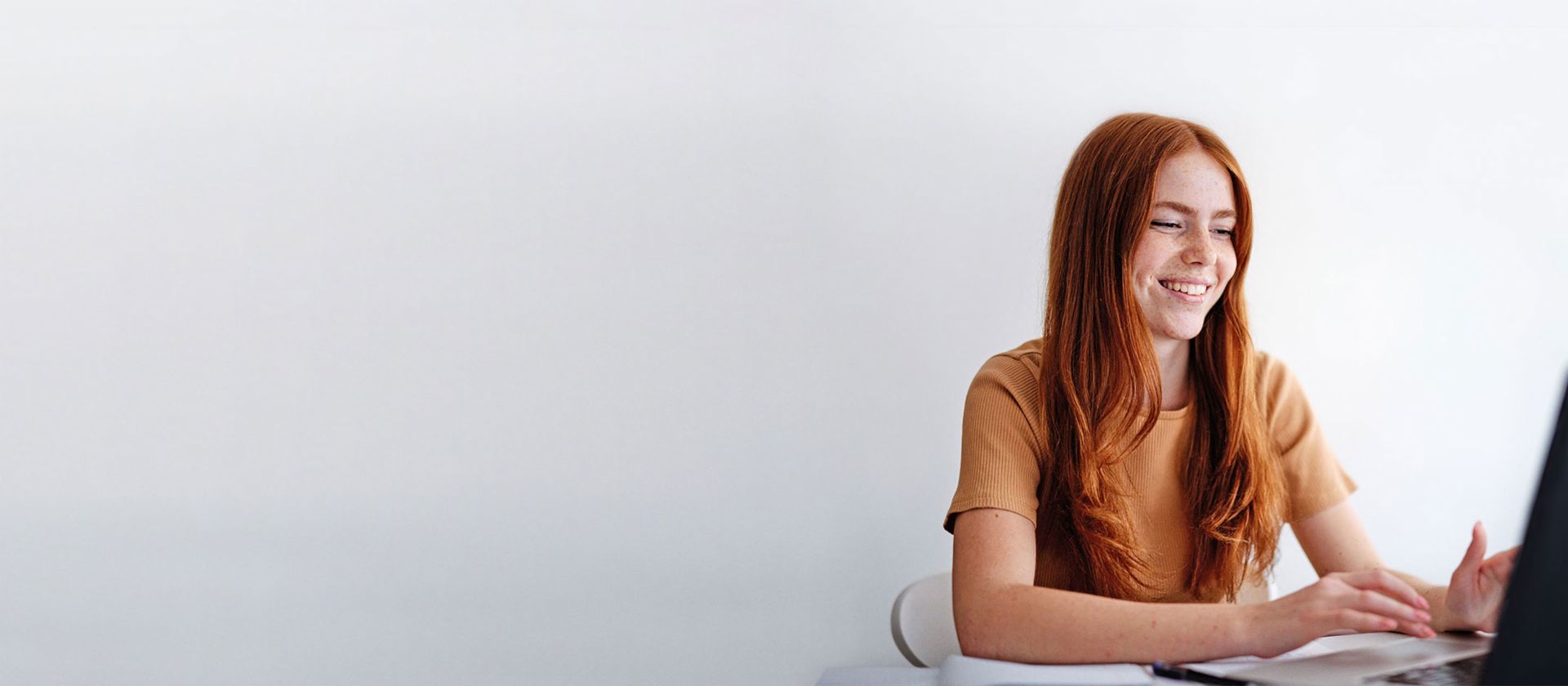 Young woman with red hair sits at the desk at the laptop.