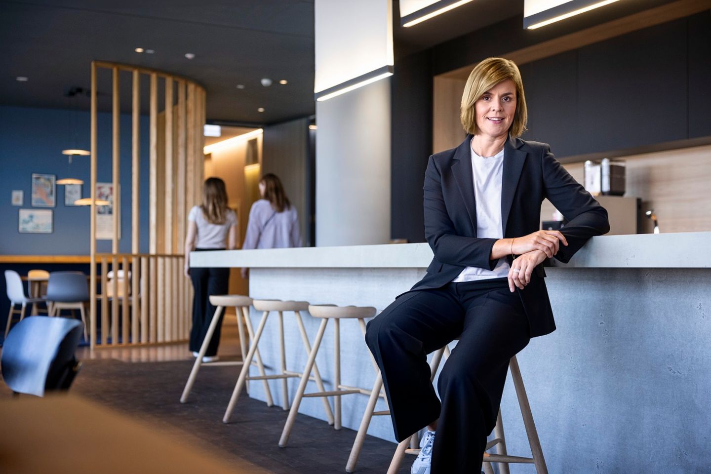 Dr. Eva Griewel, CFO al Grupului EOS, stă într-un spațiu social pe un taburet înalt, purtând un blazer negru.