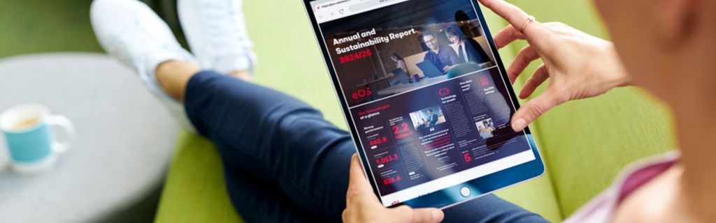 Persoană pe o canapea verde care vizualizează Raportul Anual și de Sustenabilitate EOS 2024/25 pe o tabletă