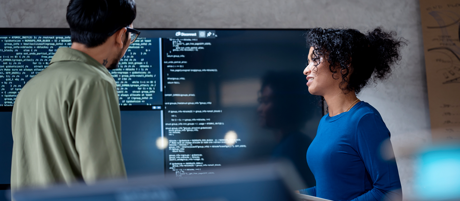 IA în recuperarea datoriilor: În această imagine, doi profesioniști analizează colaborativ codul programului pentru procese automatizate pe un ecran mare. Scena ilustrează aplicația practică a Inteligenței Artificiale (IA) și a Automatizării Proceselor Robotizate (RPA) în gestionarea datoriilor – un exemplu de transformare digitală în managementul creanțelor.