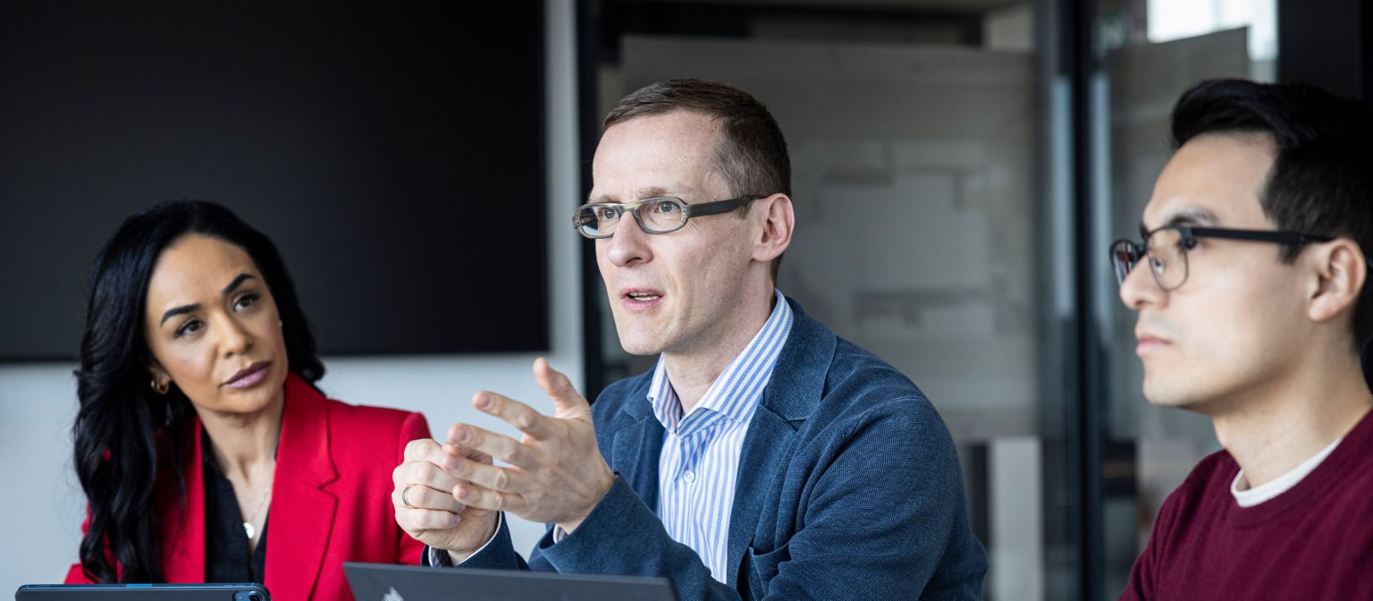 Trei persoane poartă o conversație într-un birou.