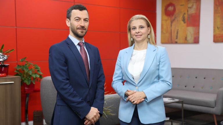 CEO Vladislav Hadjidinev in a blue suit and Katerina Bosevska Managing Director of EOS North Macedonia in a light blue blazer standing next to each other in a office with a red wall
