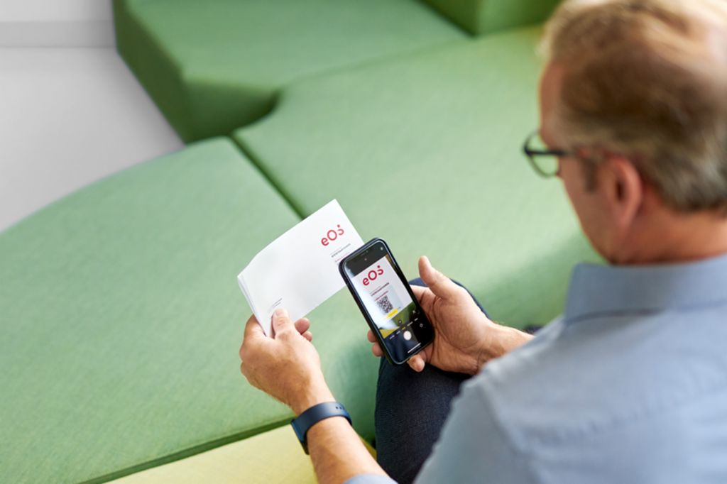 Un bărbat scanează un cod QR de pe o scrisoare de la EOS cu smartphone-ul său pentru a-și plăti creanța deschisă online pe Portalul EOS.