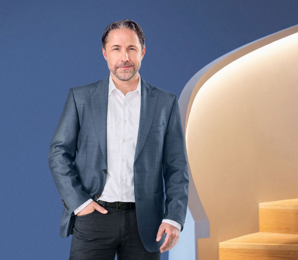 Marwin Ramcke, Director General al Grupului EOS, stă în fața unui fundal albastru, îmbrăcat într-o jachetă închisă la culoare. El privește direct în cameră.