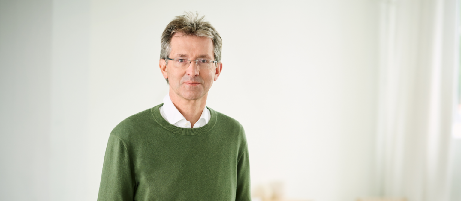 Justus Hecking-Veltman, CFO, cu pulover verde și cămașă albă, stând într-o cameră luminoasă.