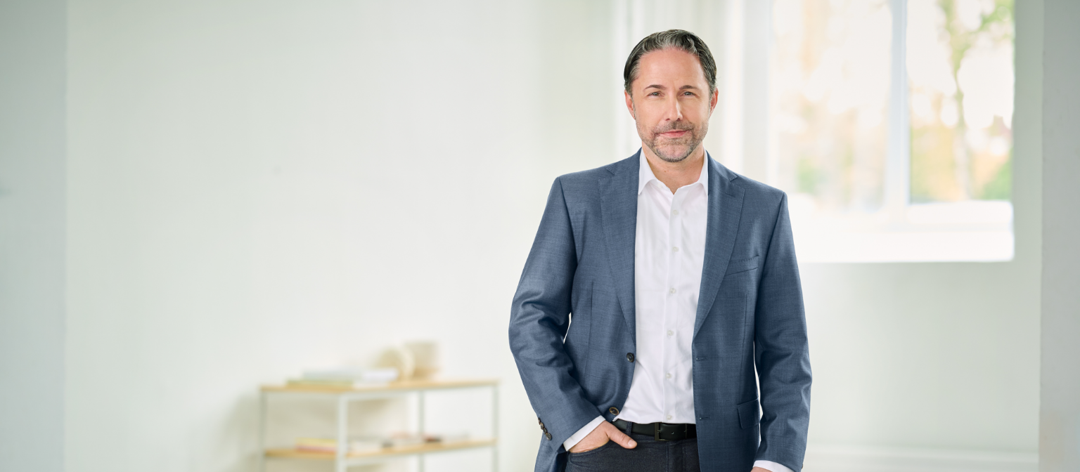 Marwin Ramcke, CEO, stând într-o cameră luminoasă, cu costum albastru și mâna dreaptă în buzunar. 