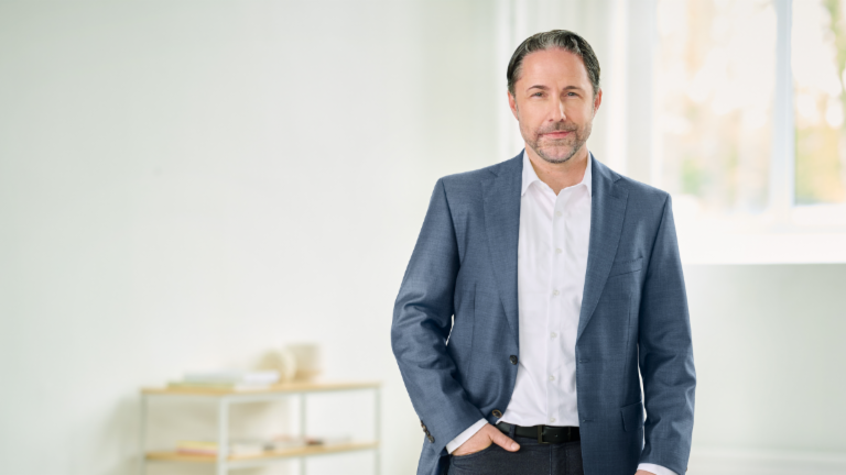 Marwin Ramcke, CEO, stând într-o cameră luminoasă, cu costum albastru și mâna dreaptă în buzunar. 